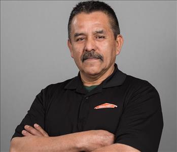 Male SERVPRO Technician with black hair smiling in front of a gray background